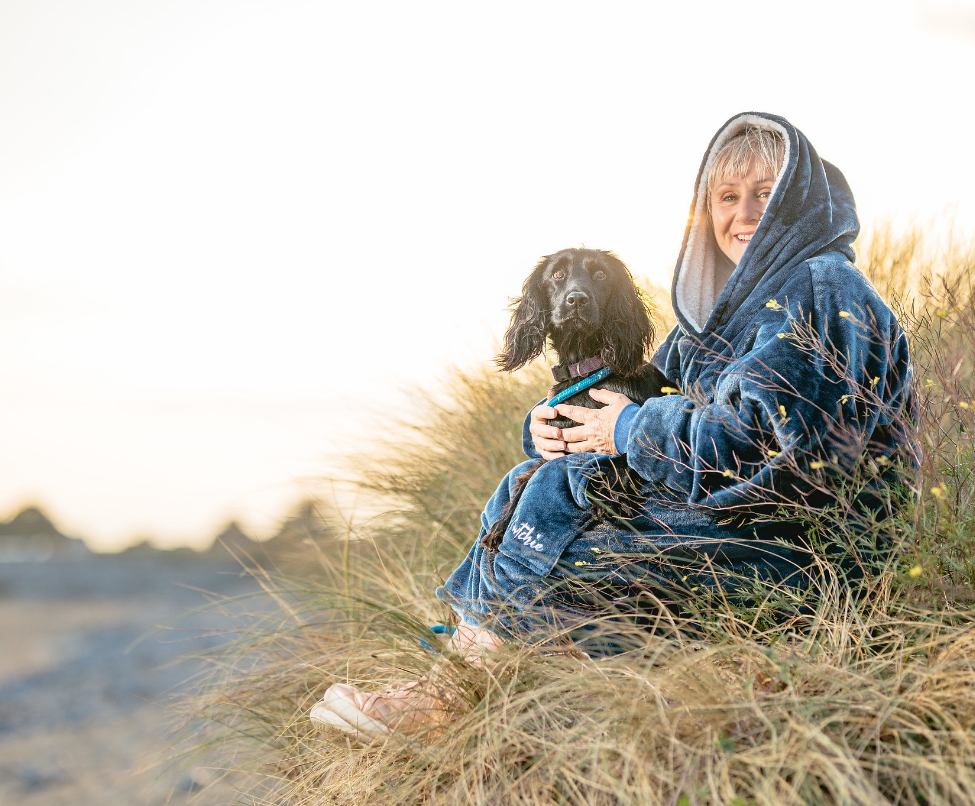 Woman with dog sittng on beach in a blue denim hoodie blanket