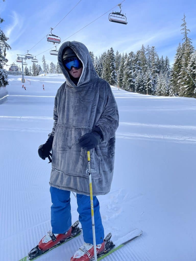 Man wearing a grey Cwtchie hoodie blanket on the ski slopes